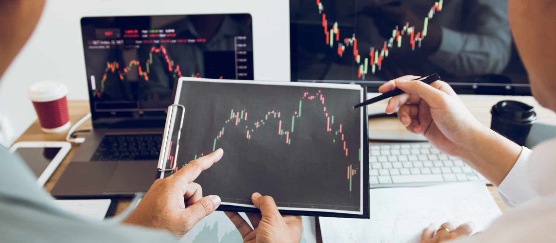 Two business stock brokers stress and looking at monitors displaying financial stock graph report information.