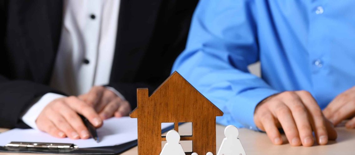 Real estate agent working with client at table, focus on house and family figures. Home insurance