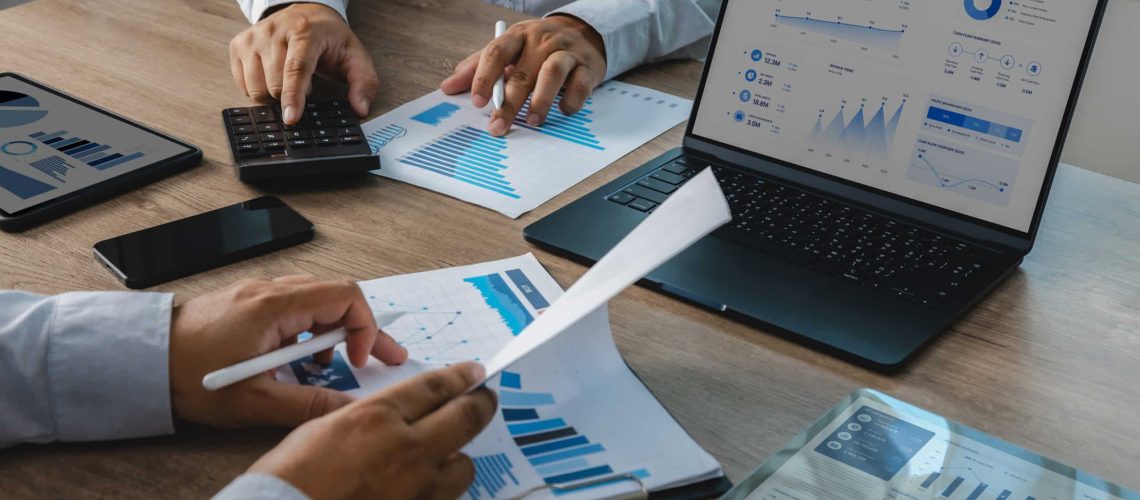 Business team reviewing accounting financial reports with calculator, charts, tablet, and dashboard on laptop during office meeting, supporting budget analysis, financial planning, and reporting workflow.