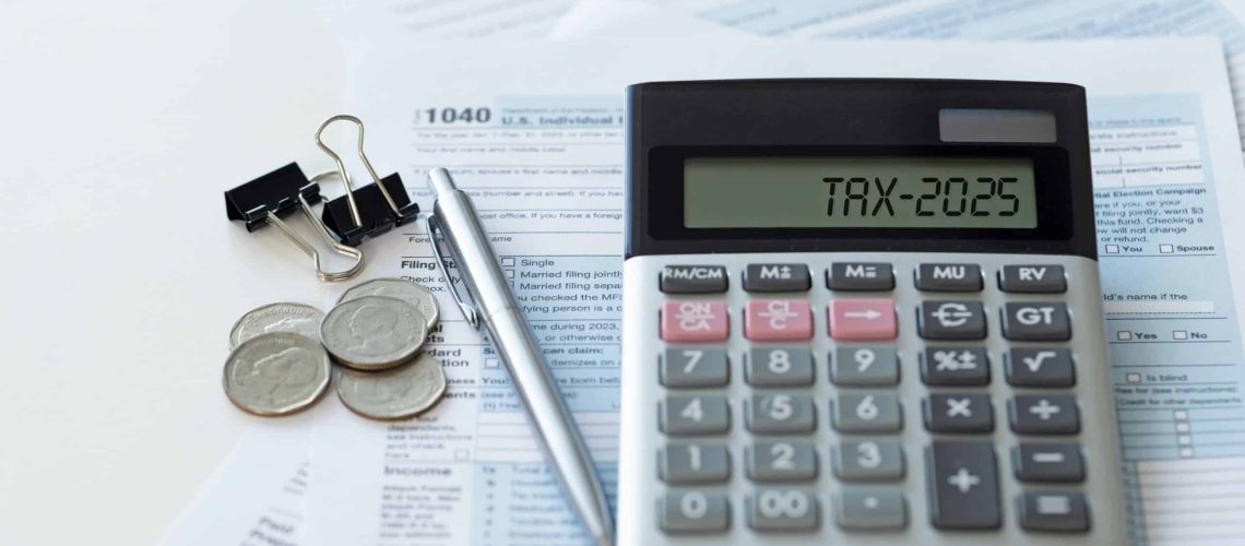 Word Tax 2025 on the calculator. Business and tax concept.Calculator, coins, form, and pen on the table.Tax deduction planning.Financial research, government taxes, and calculation of tax return