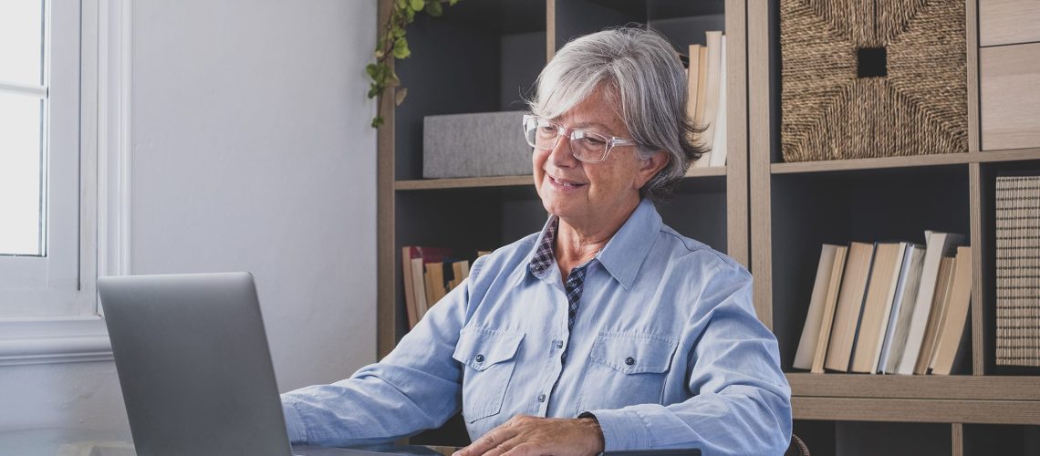 Happy old caucasian businesswoman smiling working online watching webinar podcast on laptop and learning education course conference calling make notes sit at work desk, elearning concept